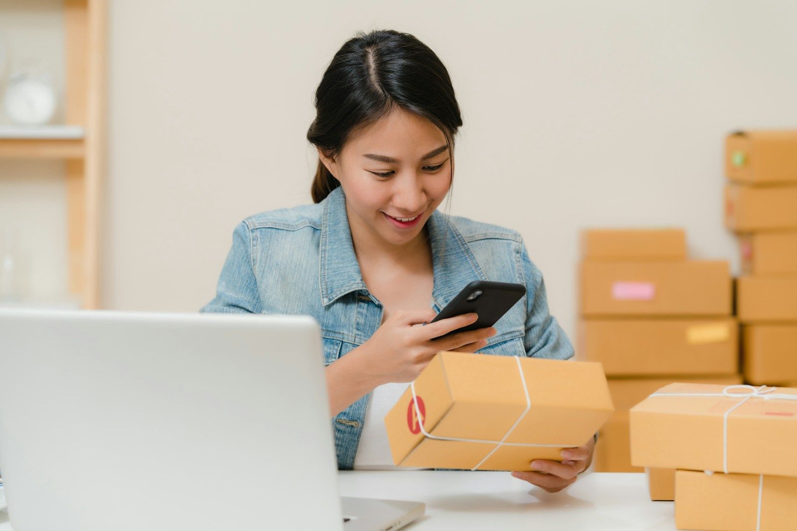 Persona revisando un paquete en el celular, con cajas de envío sobre la mesa.